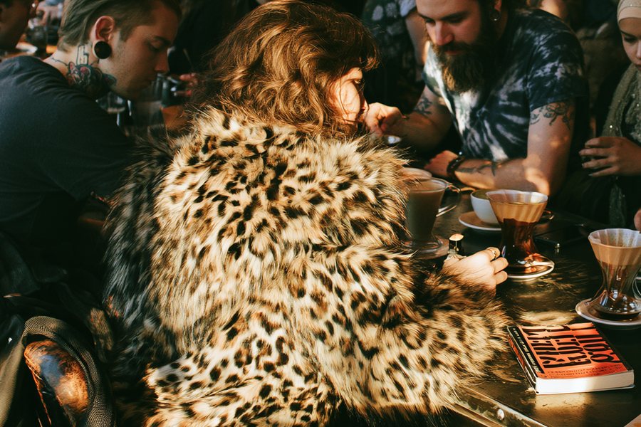 A regular in a leopard-print coat at her table with two pour-overs and a book at Cafe Socialist